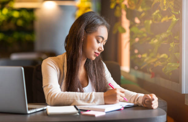 istock Young Woman Studying in a Modern Cafe, Taking Notes in a Notebook With Focused Expression 2194941654