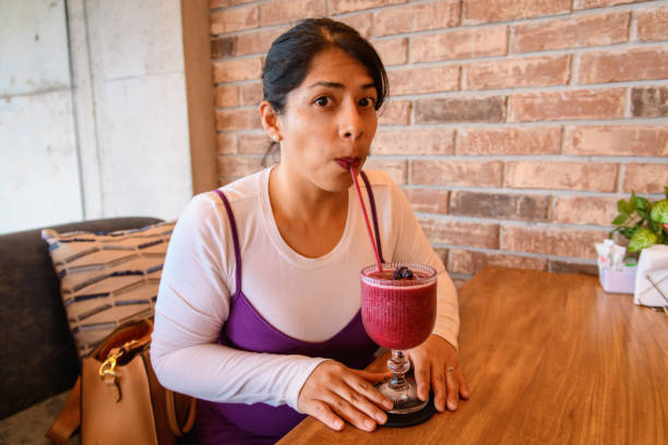 Latina Hispanic woman dressed in purple at a warm coffee shop drinking blackberry smoothie with a straw
