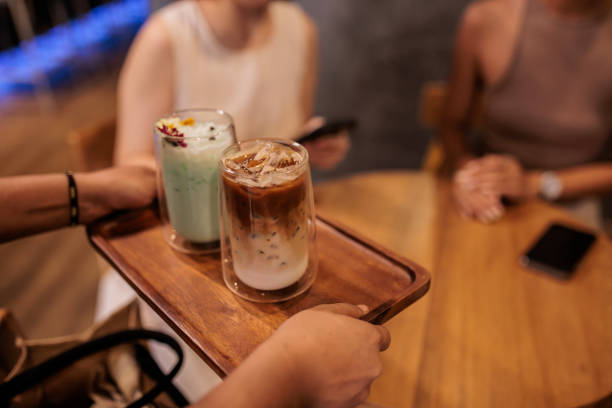 Unrecognizable waitress serving iced latte's to two Thai women at a trendy cafe.