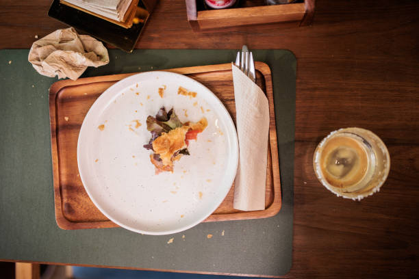 Half eaten croissant sandwich with crumbs on a plate next to iced coffee on table in cafe.