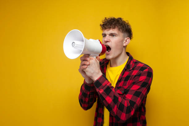 istock curly guy shouts into a megaphone on a yellow background, a student announces information 2194954689