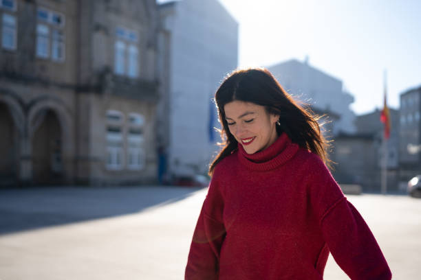 istock Mid-age woman walking confidently through urban square, sporting red turtleneck, long brown hair, bright lipstick, radiating warmth under sunlight 2194959023