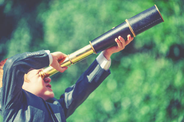 A child in a business suit looking through a telescope looking for business opportunities, forecasting, leadership and innovation