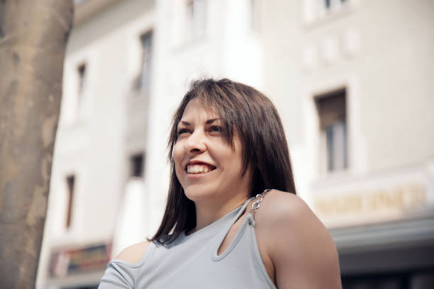 A cheerful young woman smiling in a sunny city street with soft natural light and buildings