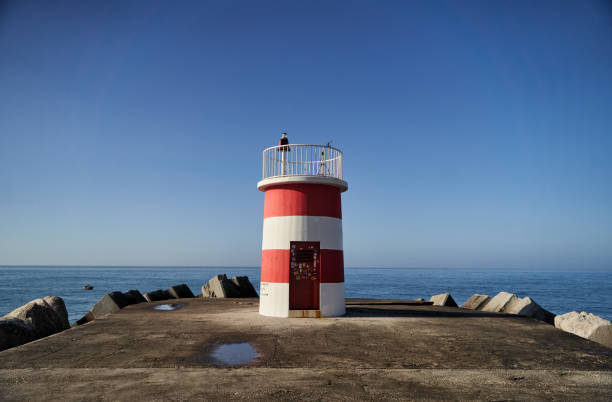 istock A Charming Lighthouse Standing Tall by the Ocean on a Bright and Clear Blue Sky Day 2194972283