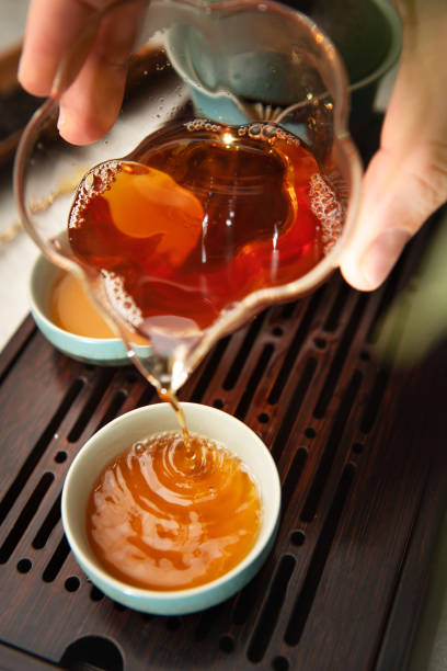 istock Female hands pouring tea from clear glass pitcher teaware into tea cups, creating serene tea ritual. Soft light, wooden tea tray evoke calming mindful Chenese ceremony atmosphere. 2194979235