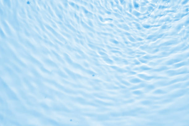 Blue water with ripples on the surface. Defocus blurred transparent blue colored clear calm water surface texture with splashes and bubbles. Water waves with shining pattern texture background.