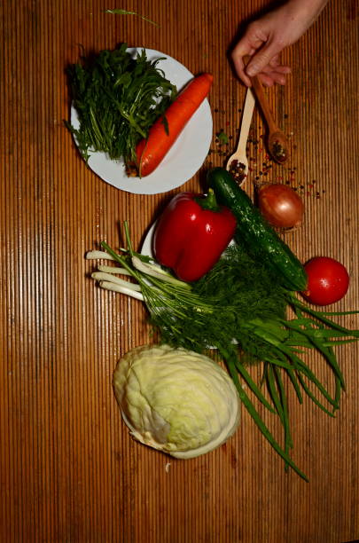 fresh vegetables of different types on a dark background for salad grass rakula tomatoes peppers wooden spoon onion cabbage carrots and other vegetables tomato, sweet pepper, greens, cucumber, light wooden spoon, onion, arugula herb with meat taste