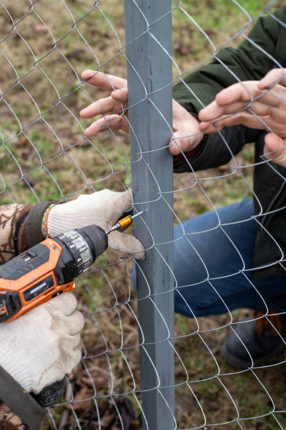 istock Workers install a chain-link fence in a garden, using a screwdriver to attach screws 2194993912
