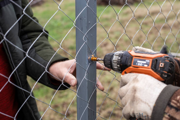 istock Workers install a chain-link fence in a garden, using a screwdriver to attach screws 2194993943