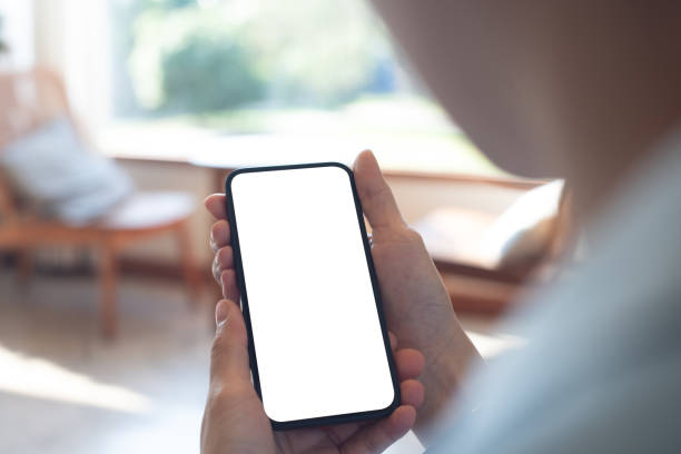 istock Mockup, woman's hands holding mobile phone with blank screen in coffee shop. Woman using smartphone, looking at the screen, over shoulder view 2195001778