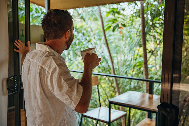 istock Man Enjoying Coffee on Balcony Surrounded by Nature 2195002229