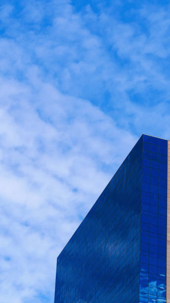 istock A modern glass building with a reflective blue facade set against a partly cloudy sky. The contrast between the solid geometric lines of the structure and the organic forms of the clouds creates a striking visual composition 2195002409