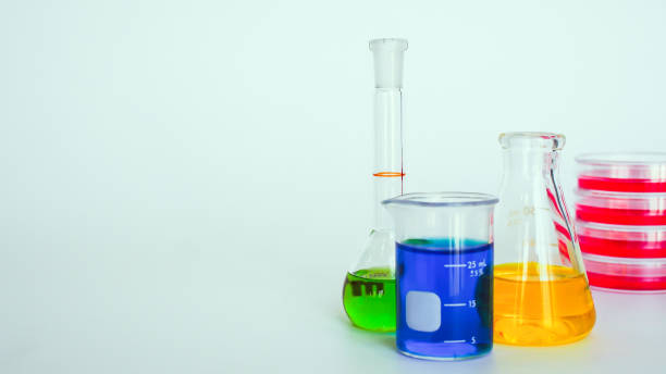 istock A close-up shot of laboratory glassware arranged on a white background, including a beaker with blue liquid, a flask with yellow liquid, a graduated cylinder with green liquid, and stacked red petri dishes. 2195002431
