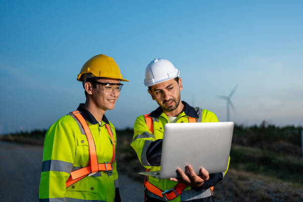 istock Diverse ethnicity male technicians working in the wind turbines field. Innovation engineer men use laptop computer work to develop environmental renewable clean energy outdoors at windmill power farm. 2195006471