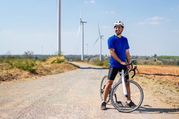 istock Caucasian man taking a break while riding bicycle at wind turbine field. Attractive athlete in sportswear exercise by cycling workout outdoors for health and wellness in rural area at windmill farm. 2195006600
