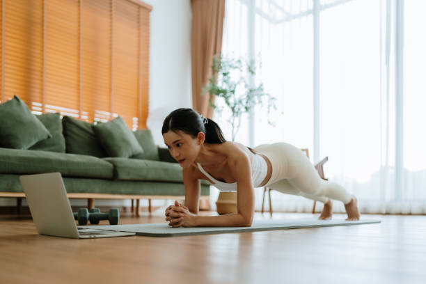 istock Young Asian woman in sportswear doing plank on training mat while watching online workout tutorials on laptop in the living room. Sport and recreation concept 2195006671