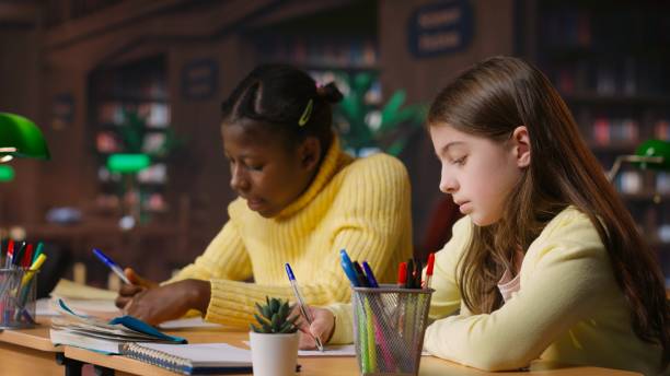 istock Caucasian tutor guiding elementary school girl at a library desk 2195008166