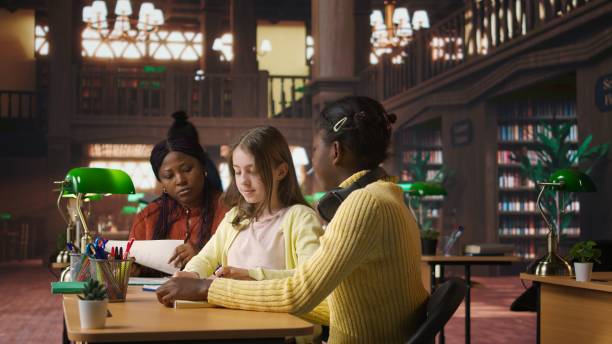 istock Preteens girls and their professor collaborating on schoolwork at the library 2195012118