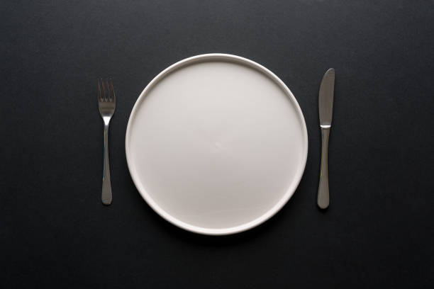 istock Top view of empty ceramic white plate and cutlery on black background 2195015515