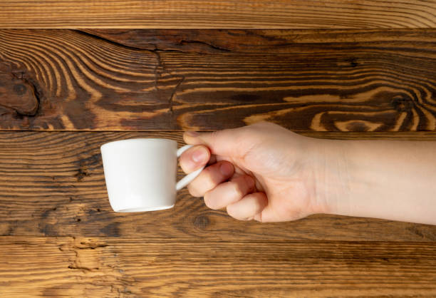 istock Hand Holds Cup, Empty White Cup in Hands, Coffee Mug, Teacup Mockup, Cup in Arms on Wooden Table 2195017684