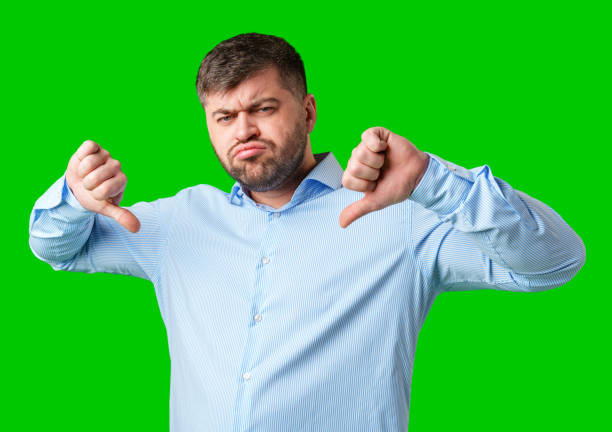 istock Man expressing disapproval with thumbs down gesture against a bright green background 2195017971