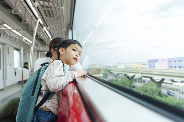 istock Asian child traveling on an elevated train, looking out the window while sitting beside his mother. 2195018809
