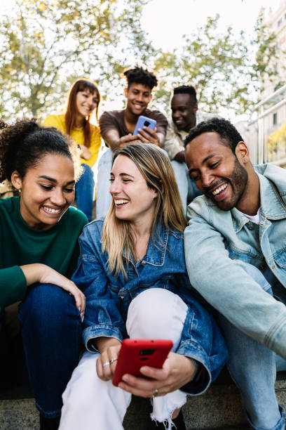 istock Young group of people sitting outdoors having fun using smartphones together 2195024583