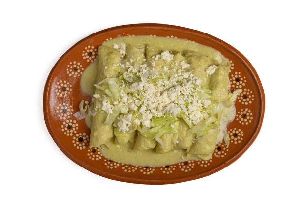 Green enchiladas with lettuce and cheese served in a clay dish on white background. stock photo