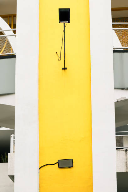 istock A tall yellow wall with a black device connected by a pole and a cable visible 2195026142
