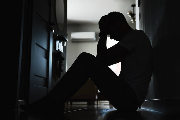Depressed man sitting on floor in dark room