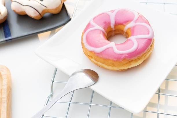 One pink doughnut on a white plate with a spoon. Sweet dessert donut for tea time.