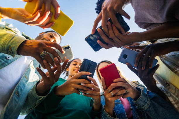 istock Young group of people using mobile phone device standing in circle outdoors 2195026575