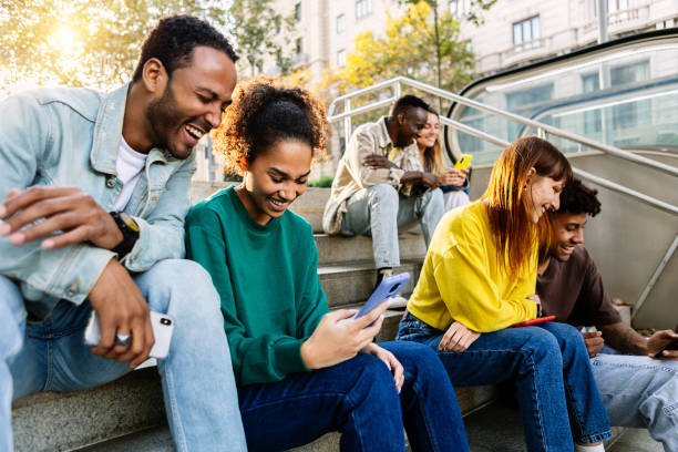 istock Group of multiracial young people using mobile phone devices sitting outdoors 2195026592