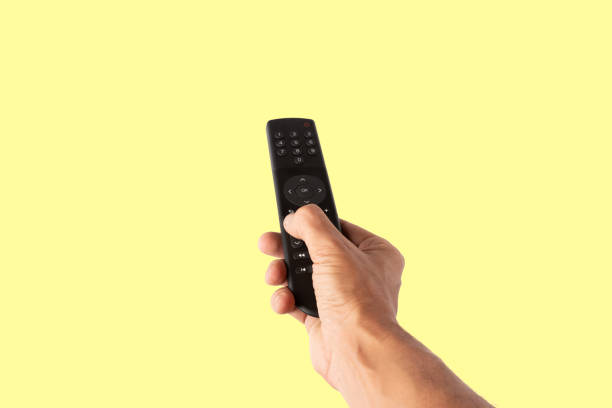 istock Male hand holding a tv remote controller isolated on yellow background cutout 2195031577