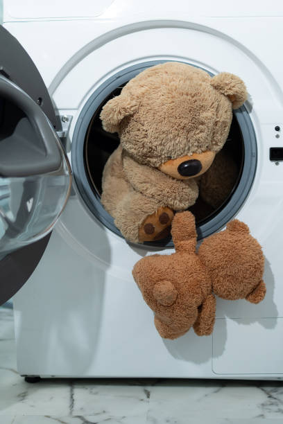istock A cute teddy bear is peeking its head out of a washing machine 2195032003