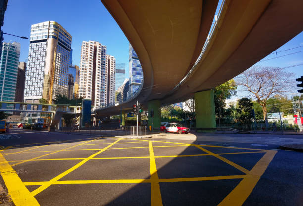 HongKong, China - January 21, 2025 : A city intersection viewed from under a highway overpass on a sunny day.  A taxi is partially visible. Yellow road markings stand out sharply against the dark asphalt.