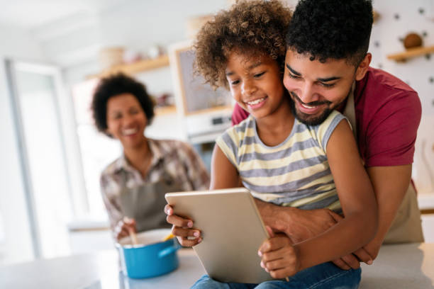 istock Happy african family having fun with device at home, using digital tablet looking at screen together 2195032706