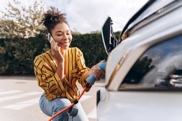 istock Happy woman inserting EV charger plug into electric car, using mobile phone at charging station 2195040813