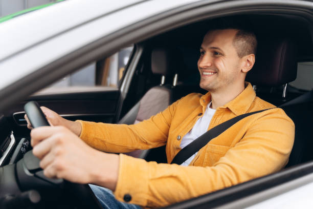 istock Smiling young man holding hands on steering wheel, using seat belt while driving car 2195040832