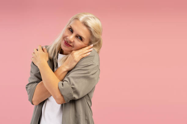 istock Smiling mature woman hugging herself on pink background 2195041129
