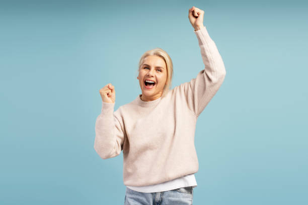 istock Excited woman celebrating with raised arms on blue background 2195041242
