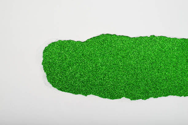 Torn white paper revealing a green glitter background. stock photo