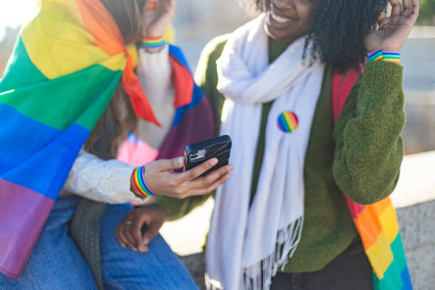 istock Two friends showing support for lgbtq plus rights, using smartphone and wearing rainbow flag 2195046345