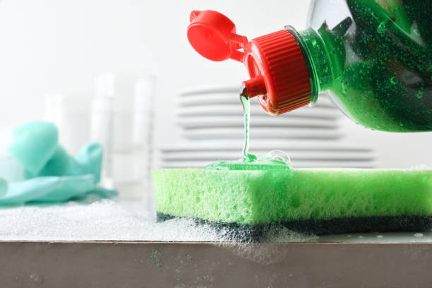 istock Pouring soap onto green scrubber with plates in the background 2195049332