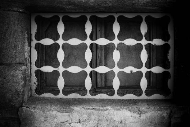 A patterned window adorned with a unique design complements the aged stone wall of the historic building. Natural light highlights the details of the intricate patterns.