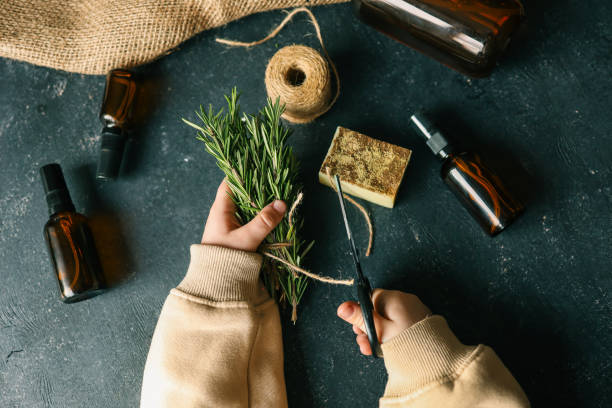 istock Child's hands cutting a bundle of rosemary with scissors on a dark surface surrounded by amber glass bottles, burlap, natural soap, and twine. Rustic and eco-friendly crafting setup with herbal elements 2195050104