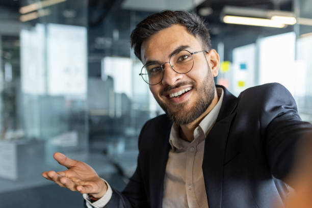 istock Video call, businessman smiling looking into smartphone camera. Man at workplace inside office in business suit working, using smartphone app for remote conversation 2195050395