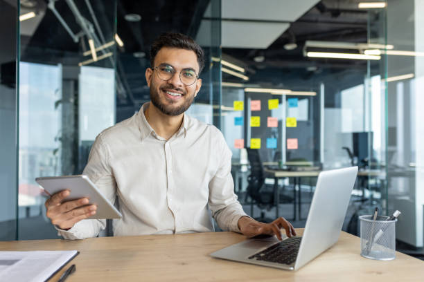 istock Latin American man working with laptop and tablet in modern office setting 2195050454