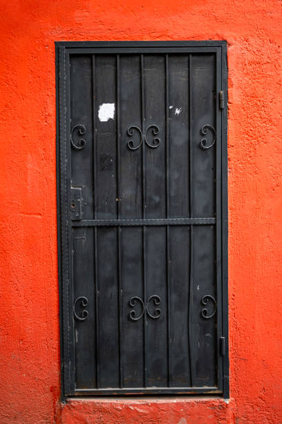 istock Black wrought iron door on vibrant orange concrete wall 2195050939